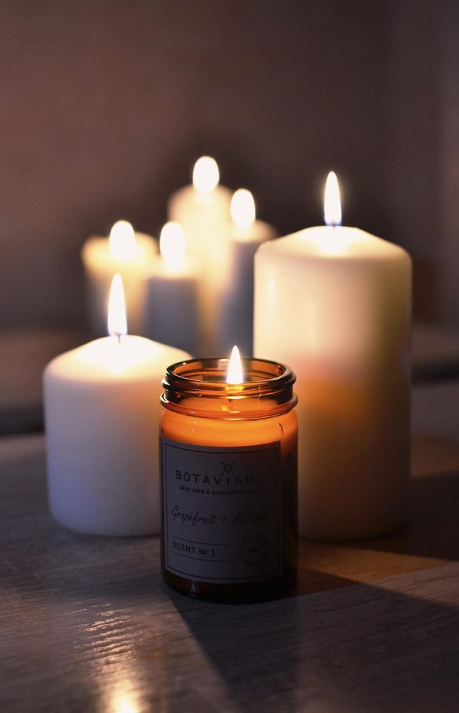 Velas acesas em diferentes tamanhos, incluindo uma aromática da marca Botavikos, criando uma iluminação suave e aconchegante. Imagem ilustrativa para post sobre como deixar a casa mais quentinha no inverno, do blog da Soma Urbanismo.