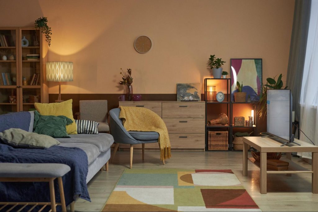 Sala de estar com iluminação quente, móveis de madeira, almofadas coloridas e decoração que transmite sensação de acolhimento. Imagem ilustrativa para post sobre como deixar a casa mais quentinha no inverno, do blog da Soma Urbanismo.