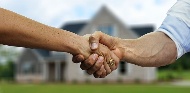 Duas pessoas dando um aperto de mão em frente a uma casa para ilustrar o post sobre fundo imobiliário da Soma Urbanismo