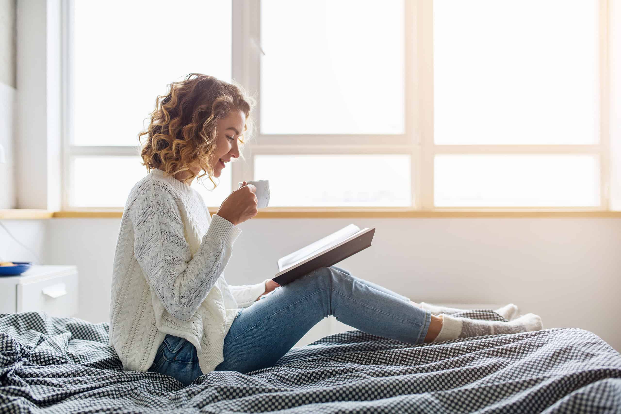 Foto de uma mulher lendo um livro e segurando uma caneca para ilustrar o texto sobre o que fazer no inverno do blog da Soma Urbanismo