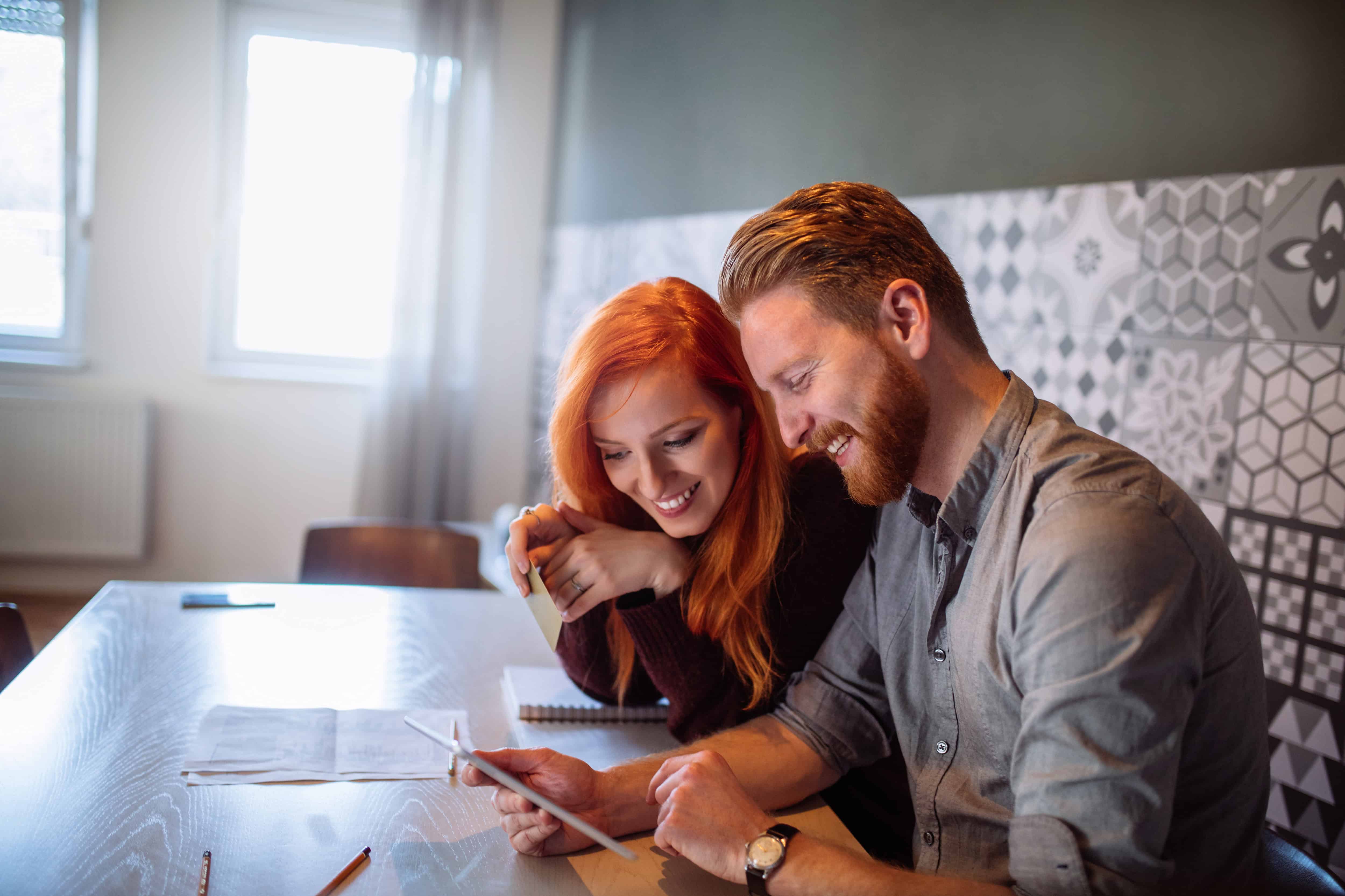 Casal sorrindo e olhando o tablet com a mão esquerda para ilustrar o texto sobre contrato digital da Soma Urbanismo