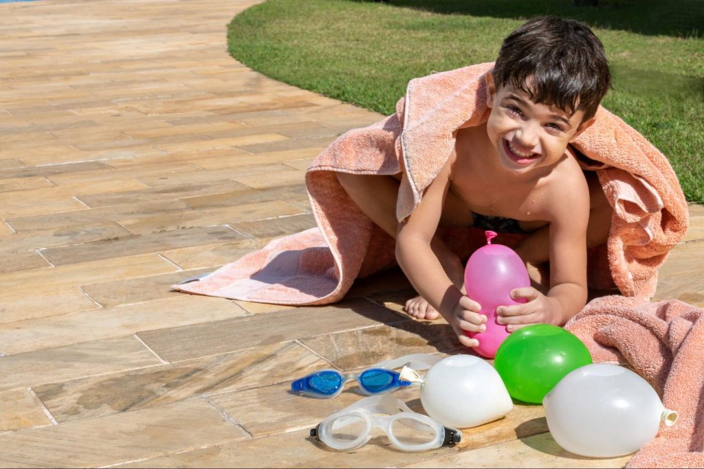Foto de um menino segurando bolas d'água para ilustrar o texto sobre brincar com as crianças no quintal. 