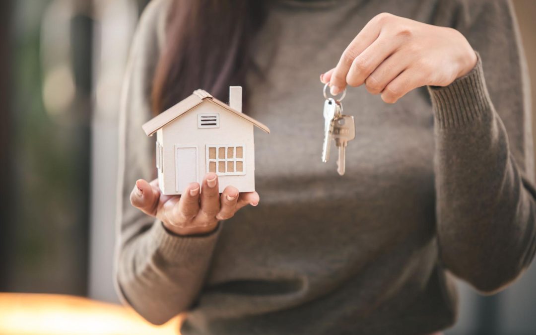 Mulher segurando casa em miniatura e chave. Imagem ilustrativa para post sobre como escolher o lote perfeito.
