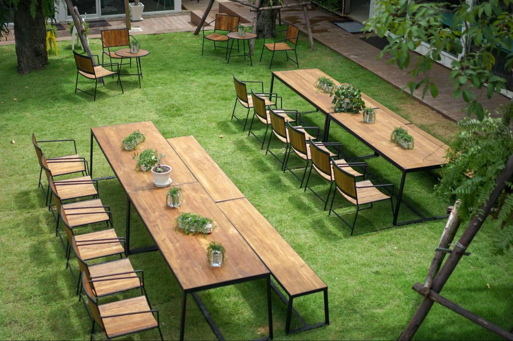 Jardim de casa com bancos e mesas de madeira. Imagem ilustrativa para post sobre paisagismo moderno.