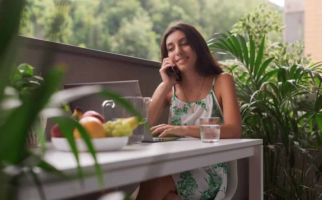 Mulher fala ao telefone em meio às plantas e frutas.