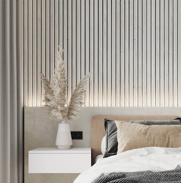 Cabeceira com ripas de madeira claras iluminadas, mesa de apoio branca e vaso com capim-dos-pampas em quarto minimalista bege.