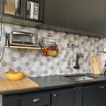 Cozinha moderna com armários pretos, bancada escura e backsplash de pastilhas hexagonais cinza atrás da pia. Imagem ilustrativa para post sobre adesivo de parede, do blog da Soma Urbanismo.
