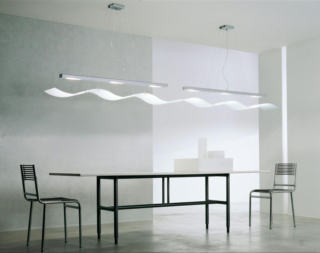 Ambiente minimalista com mesa retangular, duas cadeiras metálicas, luminárias pendentes modernas e decoração em tons claros. Imagem ilustrativa para post sobre tendências de decoração ultrapassadas, do blog da Soma Urbanismo.