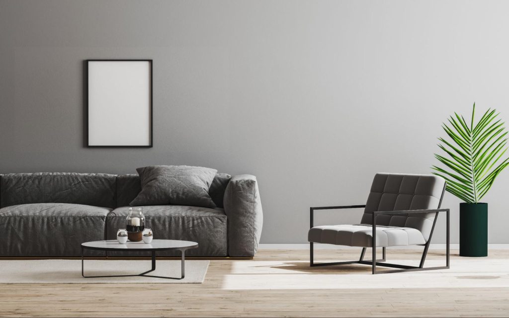 Sala de estar minimalista com sofá cinza, poltrona moderna, mesa de centro baixa e planta decorativa em vaso preto, com parede e quadro em tons neutros. Imagem ilustrativa para post sobre tendências de decoração ultrapassadas, do blog da Soma Urbanismo.